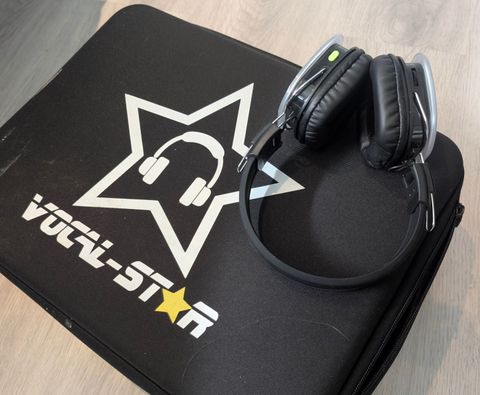 A black over-ear silent disco headset with a green power light, resting on its black carry case